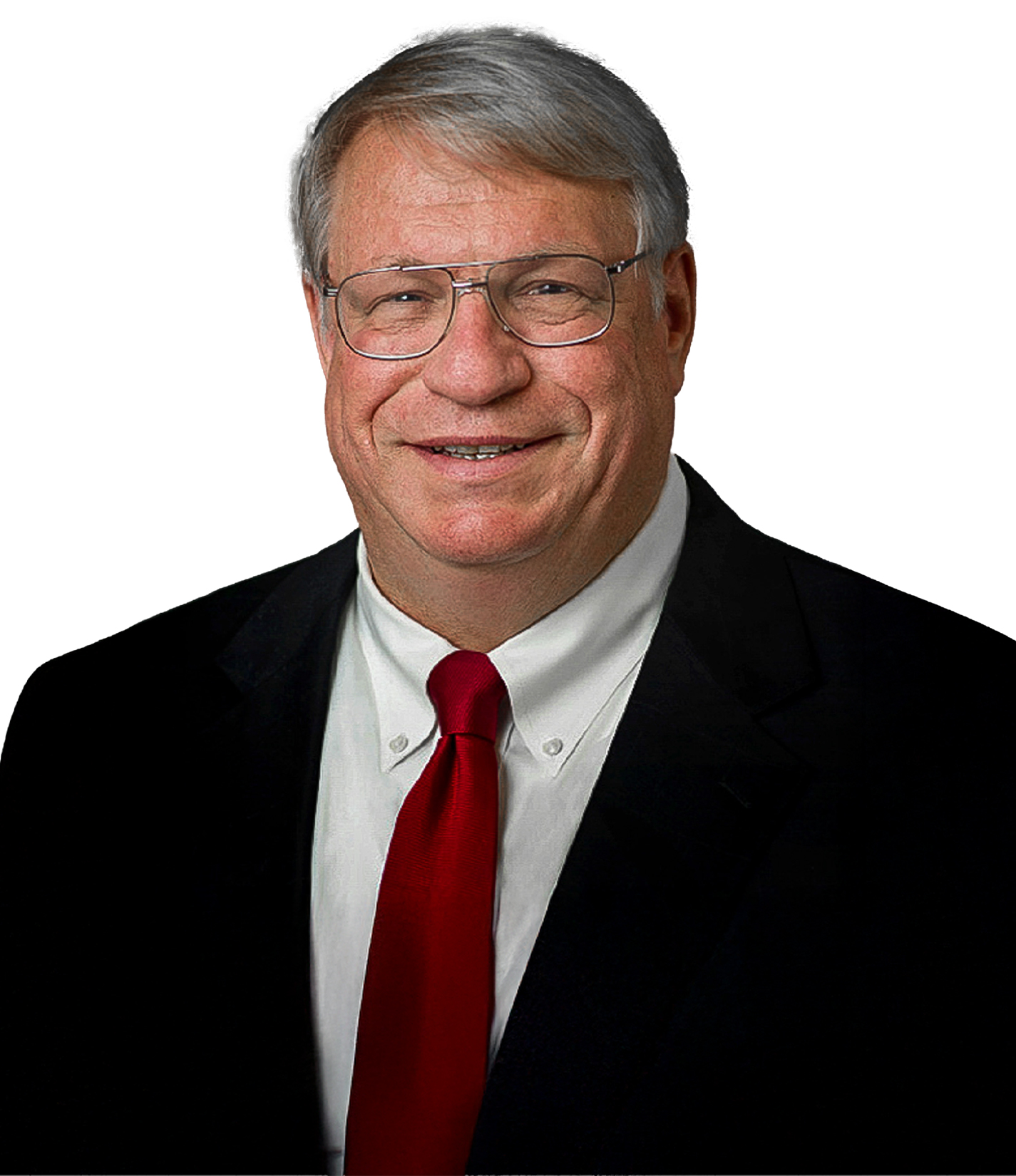 A man with short gray hair and glasses wearing a black suit, white shirt, and red tie, smiling against a white background.