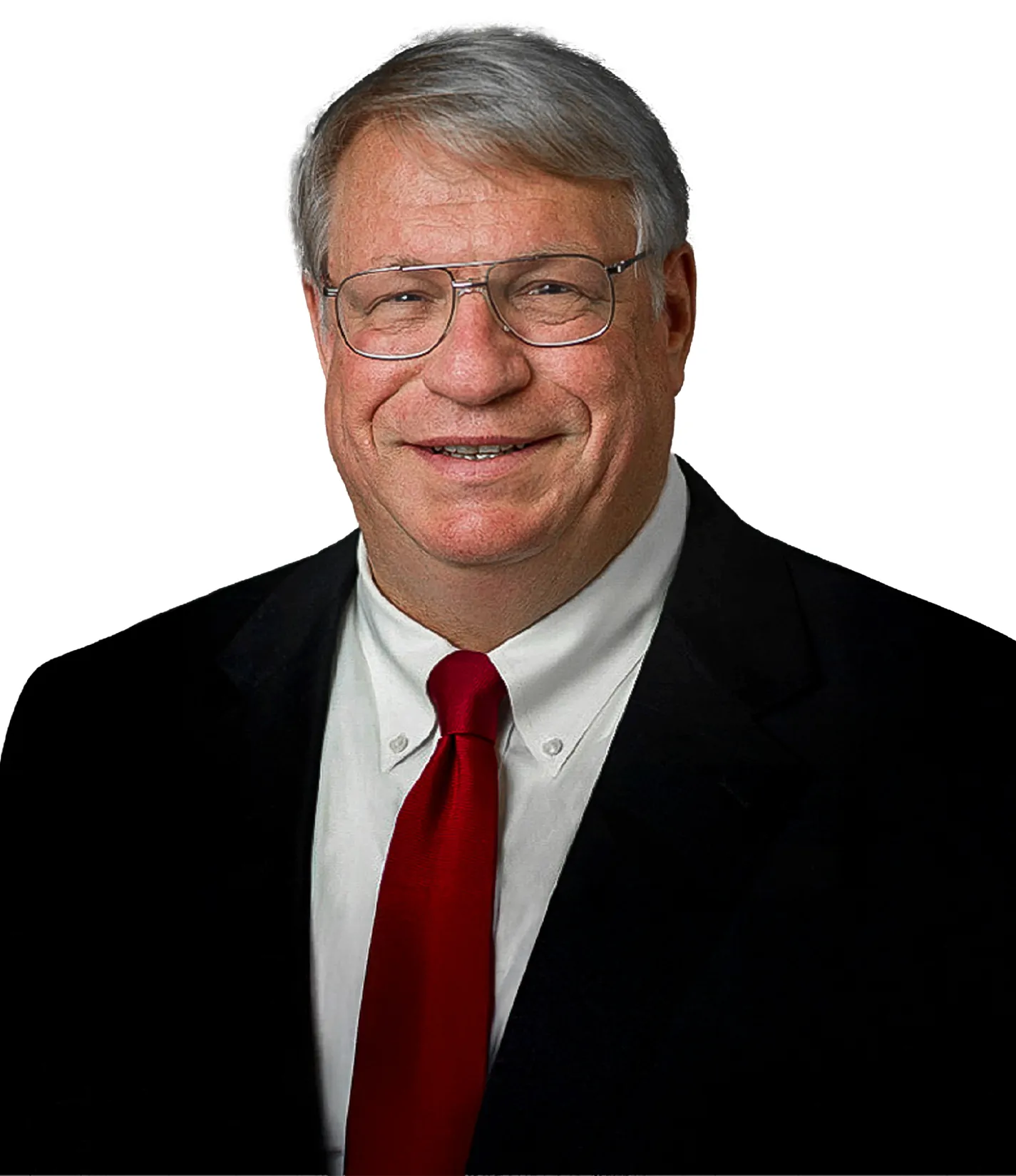 A man with short gray hair and glasses wearing a black suit, white shirt, and red tie, smiling against a white background.