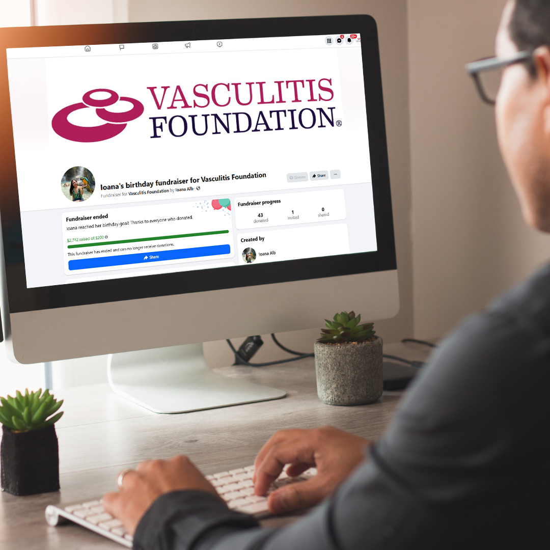 A person sits at a desk using a desktop computer displaying a Facebook fundraiser page for the Vasculitis Foundation. The screen shows the Vasculitis Foundation logo at the top and a completed birthday fundraiser with donor progress.