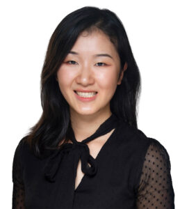 A woman with shoulder-length dark hair wearing a black blouse with a tie detail at the collar, smiling against a white background.