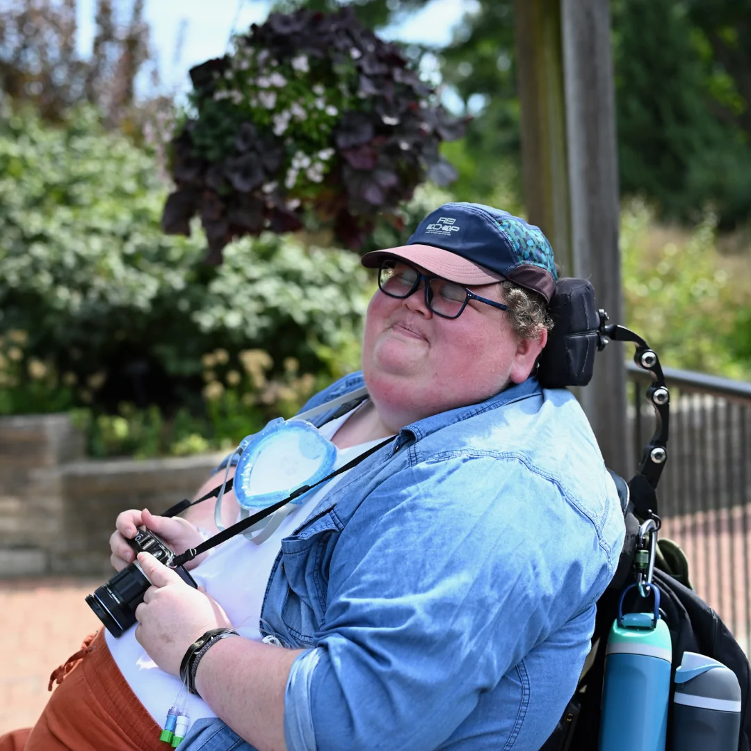 Annesley Clark pictured outdoors in a natural setting, smiling and holding a camera.