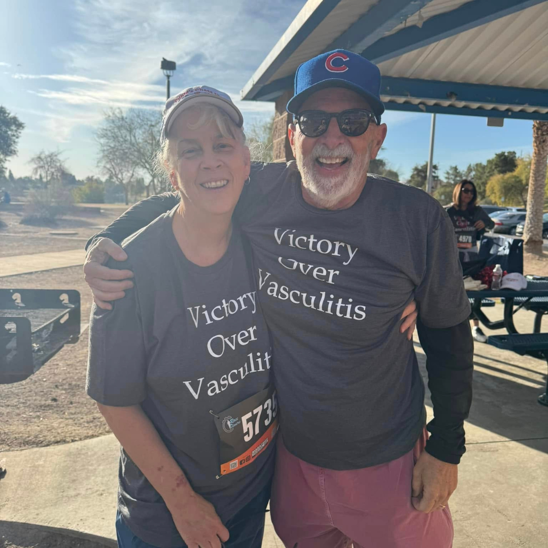 Irene, pictured smiling outdoors with a loved one, wearing a Vasculitis Foundation t-shirt.