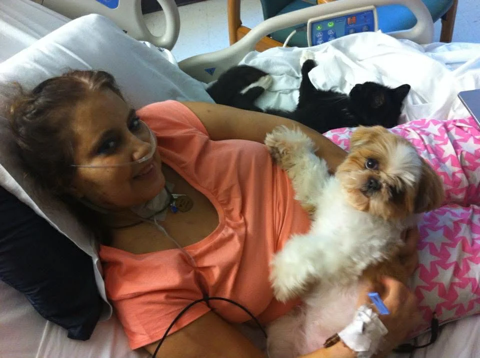 Carmen P. pictured in a hospital bed with her dog smiling