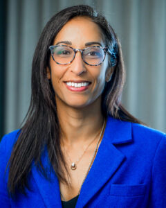 Professional headshot of a woman wearing glasses and a blue blazer, smiling at the camera.