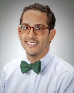 Headshot of a man wearing glasses and a green bow tie with a light-colored shirt.