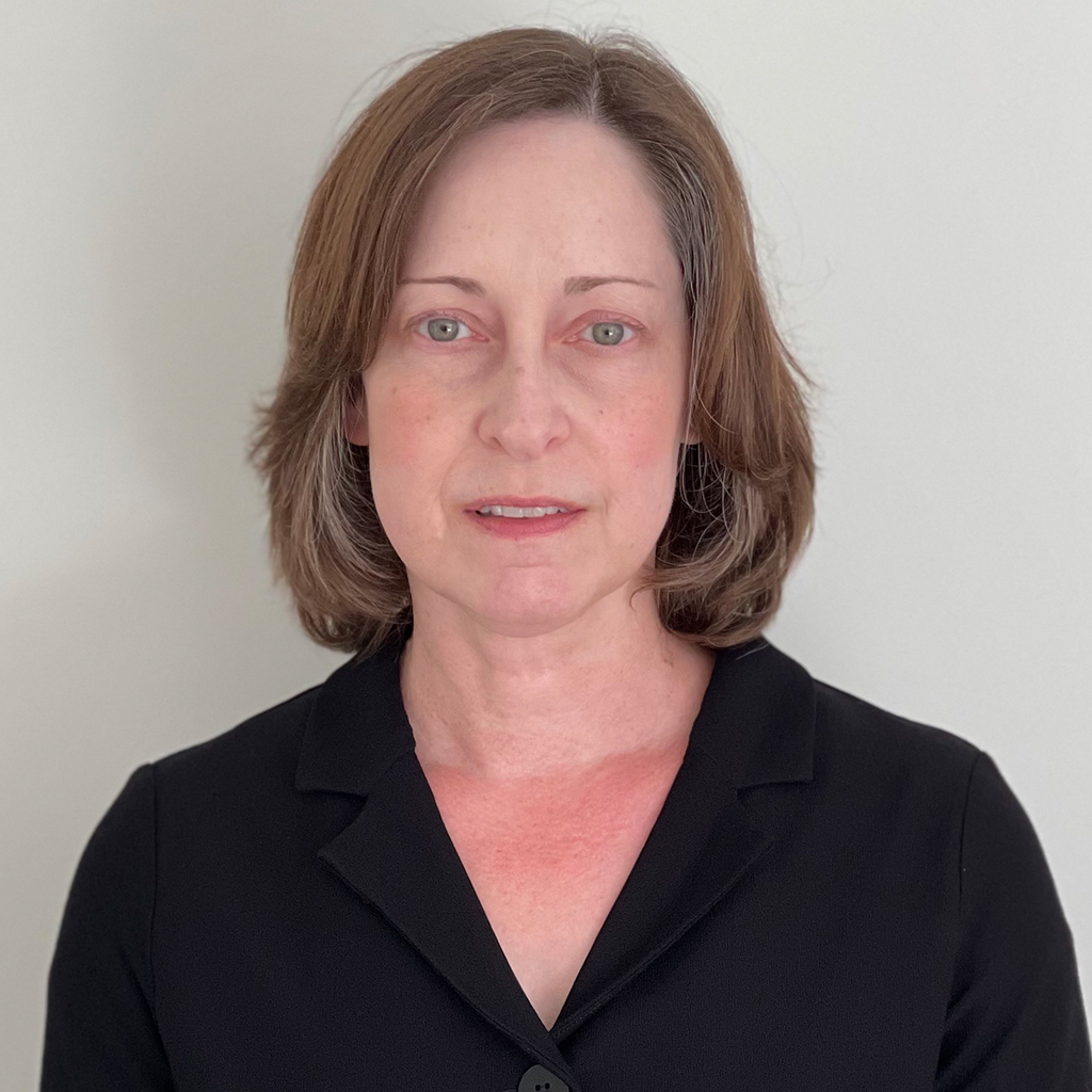 Woman with short light brown hair wearing a black blazer, facing forward against a plain light background.