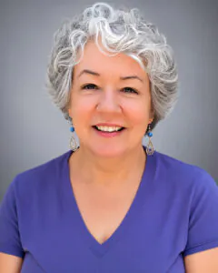 Smiling woman with short curly gray hair wearing a purple top