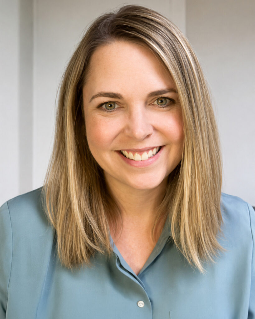 Headshot of a smiling woman with shoulder-length blonde hair, wearing a teal blouse, against a light neutral background.
