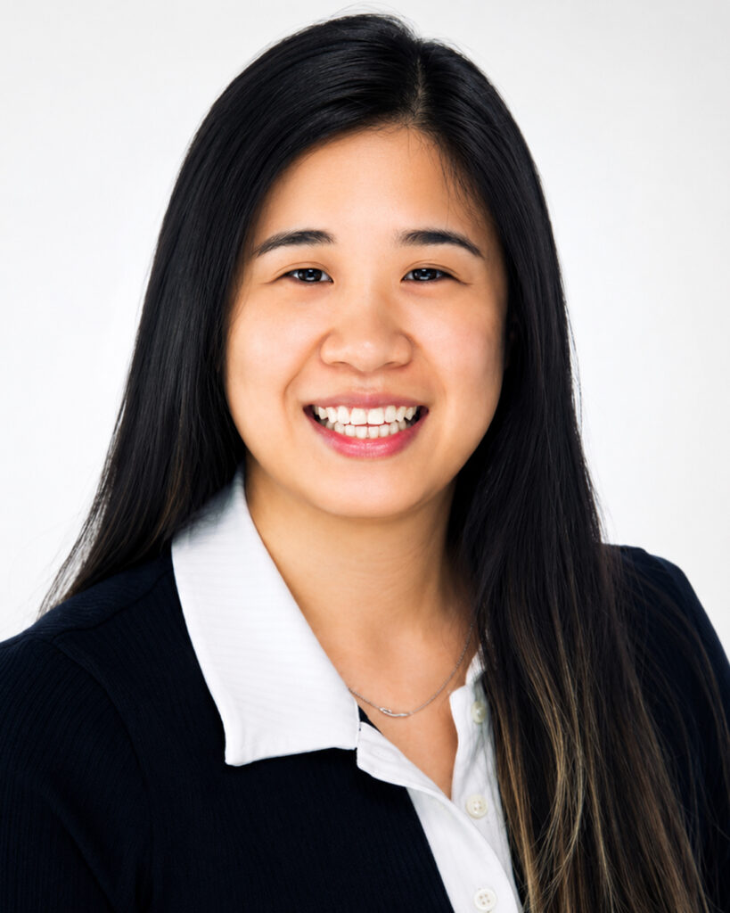 Professional headshot of a smiling Asian woman with long dark hair, wearing a dark blazer over a white collared blouse, against a clean light gray background.