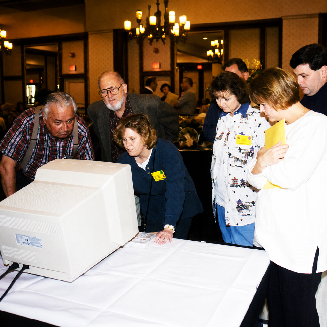 Archival photograph of several people gathered around a large desktop computer during a conference, leaning forward to view the screen.