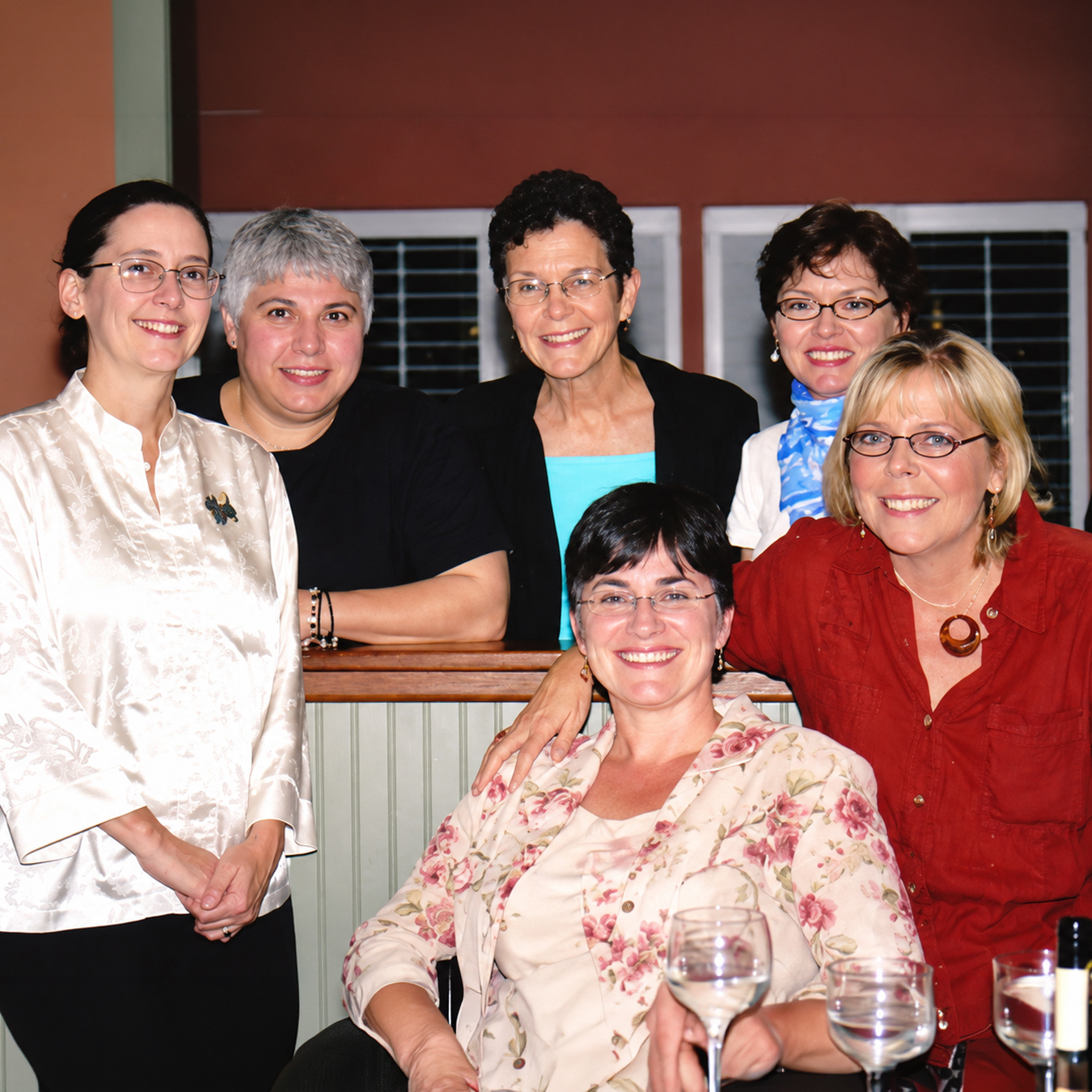 Six women pose together indoors at a gathering, smiling at the camera, with Joyce Kullman standing second from the left.