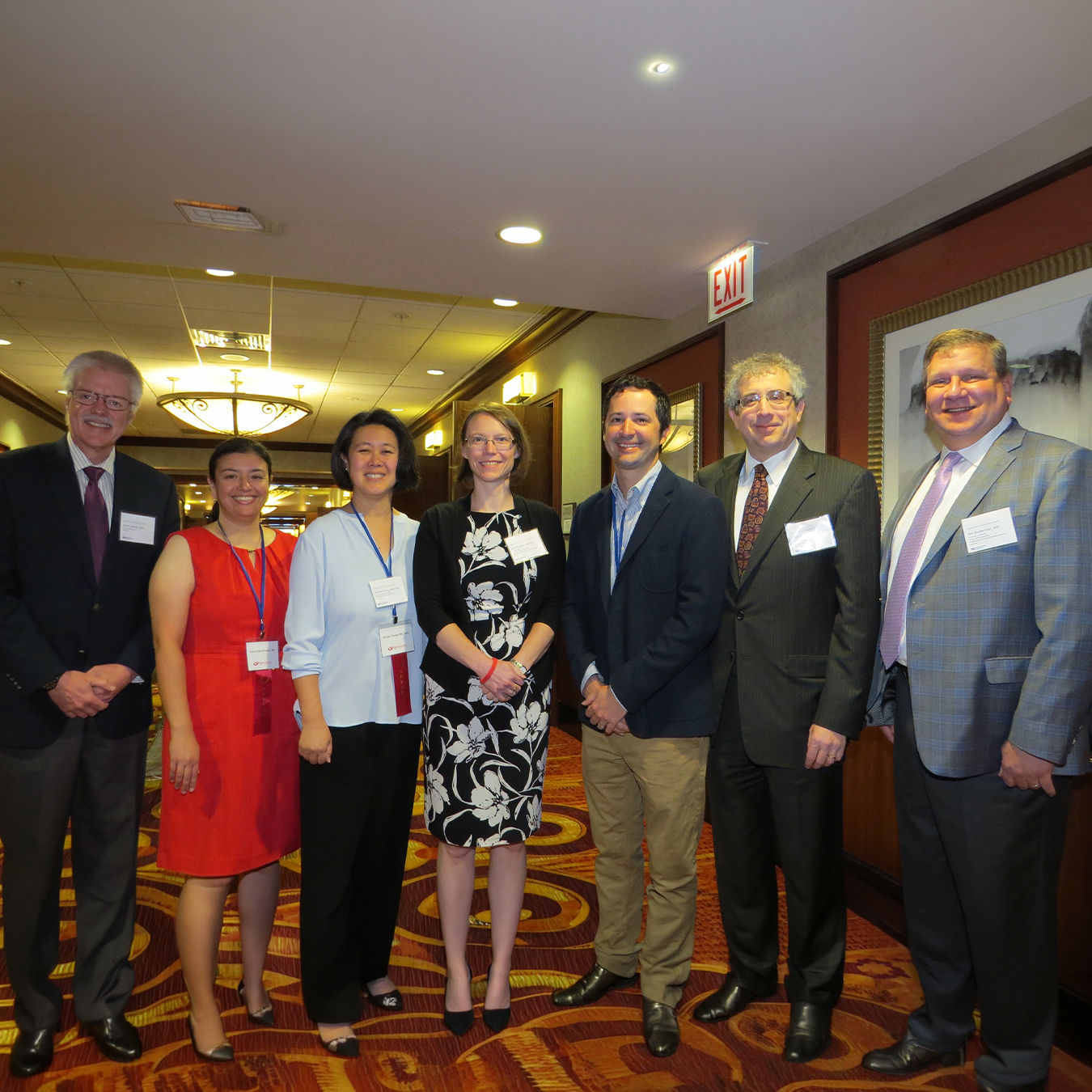 Seven medical professionals and presenters wearing conference badges pose together in a hotel hallway during the 2017 Vasculitis Symposium in Chicago.