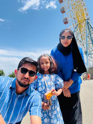 Sahala pictures at a carnival with her husband and daughter with a ferris wheel in the background.