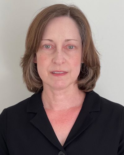 Woman with short light brown hair wearing a black blazer, facing forward against a plain light background.